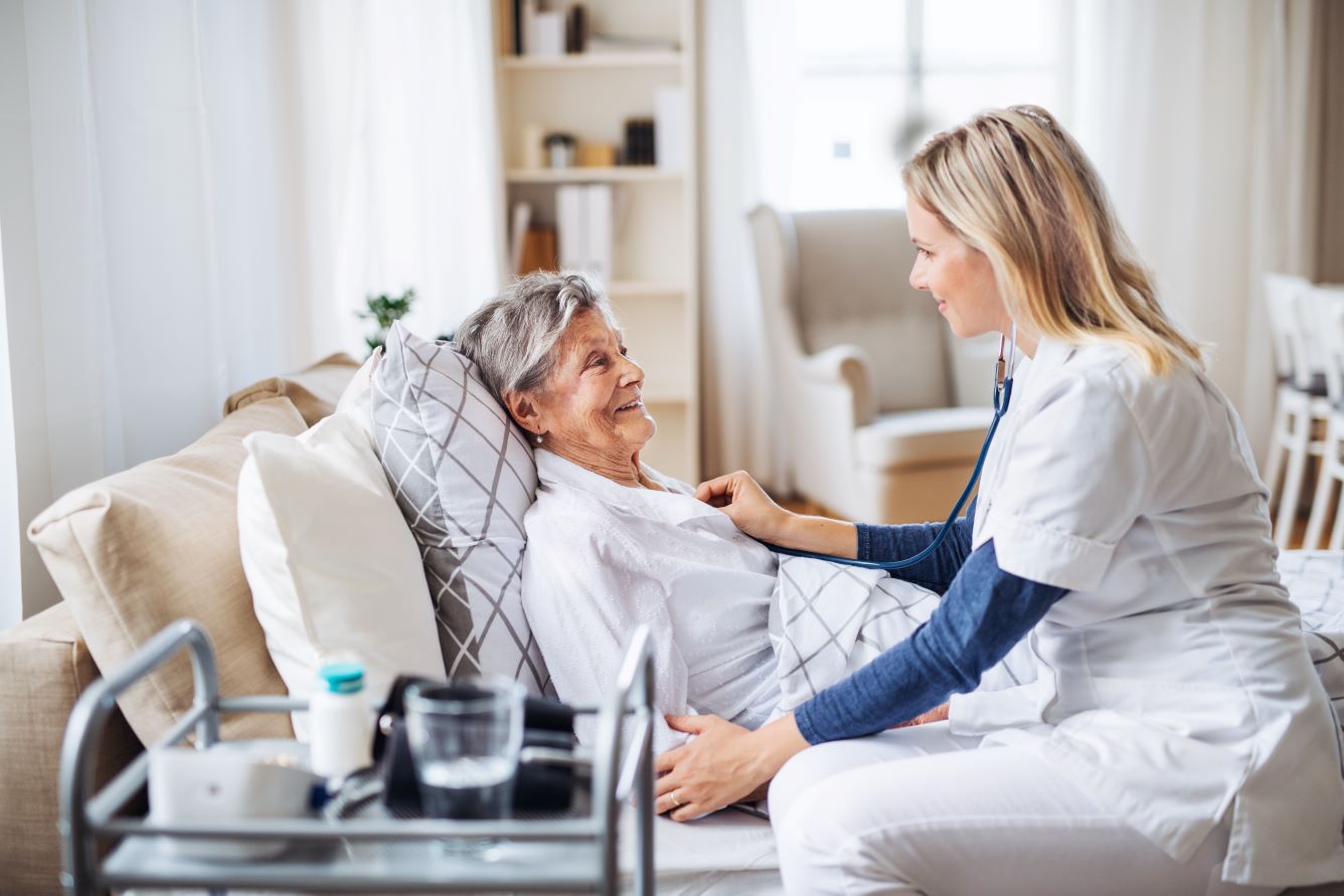 A healthcare professional caring for a senior patient lying in bed at home
